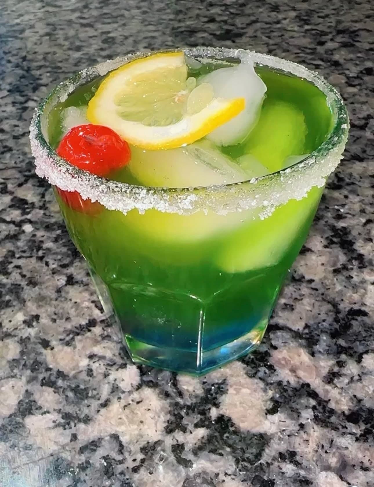 Green signature cocktail with lemon and cherry garnish